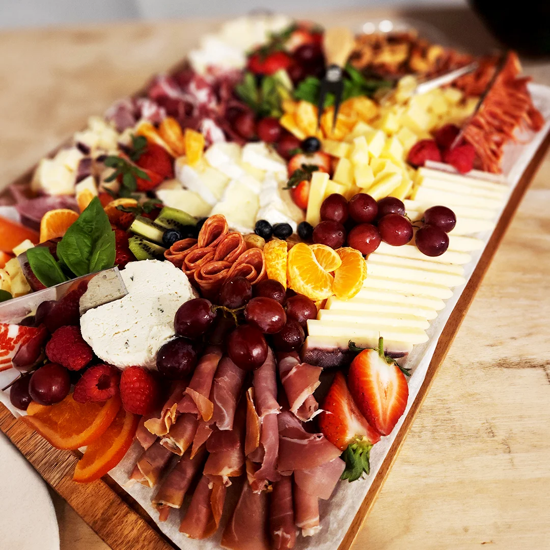 Charcuterie board featuring assorted cheeses, cured meats, fresh fruit, and garnishes arranged for a catered event.