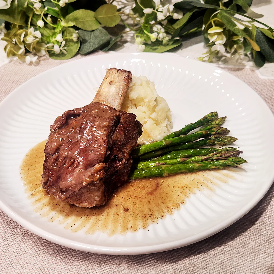 Braised short rib served with mashed potatoes, asparagus, and pan sauce on an elegant dinner plate.