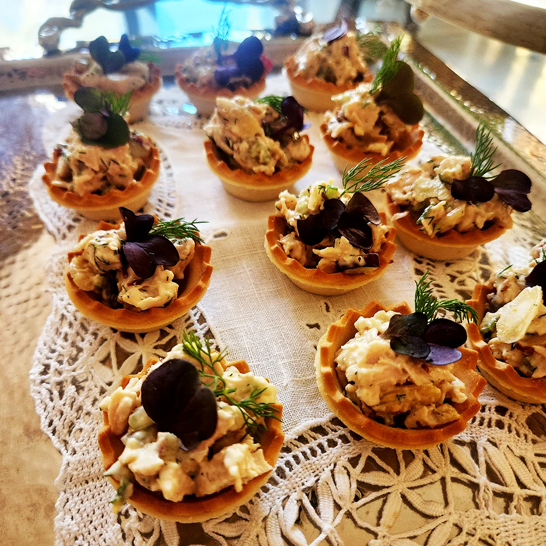 Bite-sized tartlet appetizers filled with chicken salad and garnished with fresh herbs and microgreens.