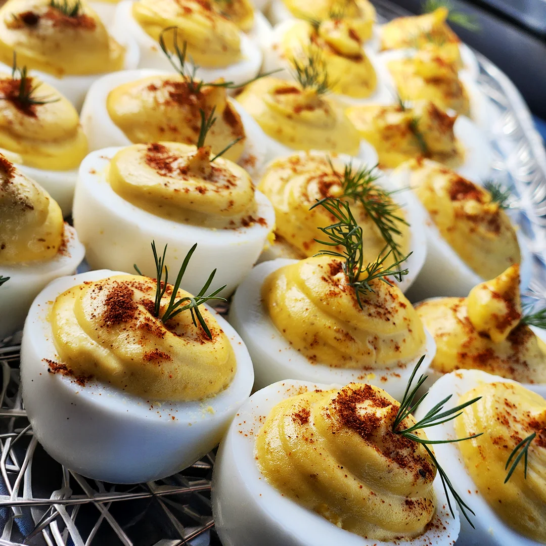 Deviled eggs topped with paprika and fresh dill arranged on a serving platter for a catered event.