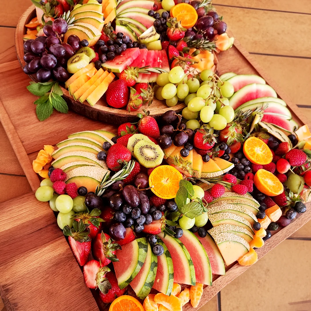 Colorful fruit grazing board featuring watermelon, melon, grapes, strawberries, kiwi, berries, and citrus arranged for a catered event.