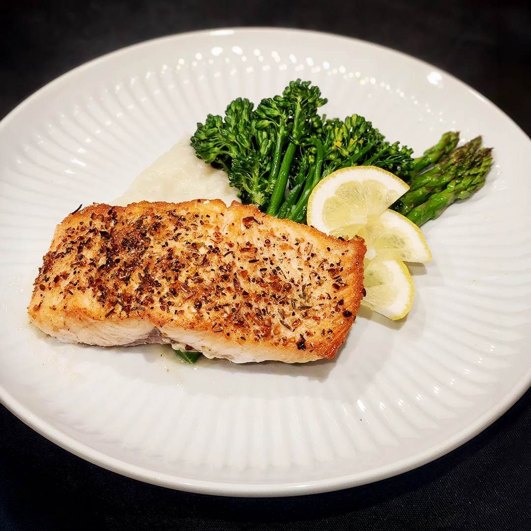 Herb-crusted salmon served with mashed potatoes, broccolini, asparagus, and fresh lemon slices.