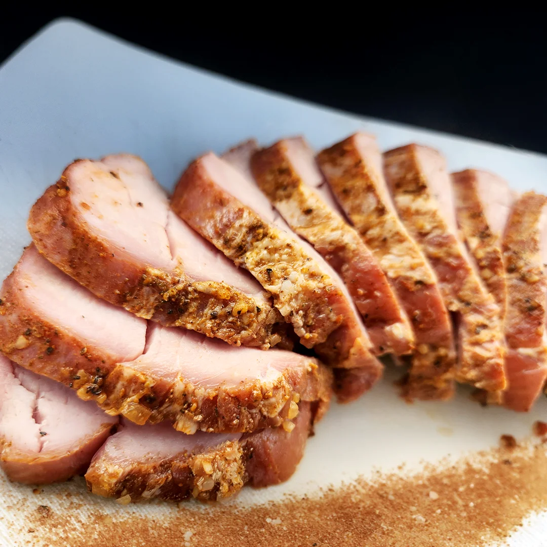 Sliced smoked pork tenderloin seasoned with herbs and spices on a serving platter.